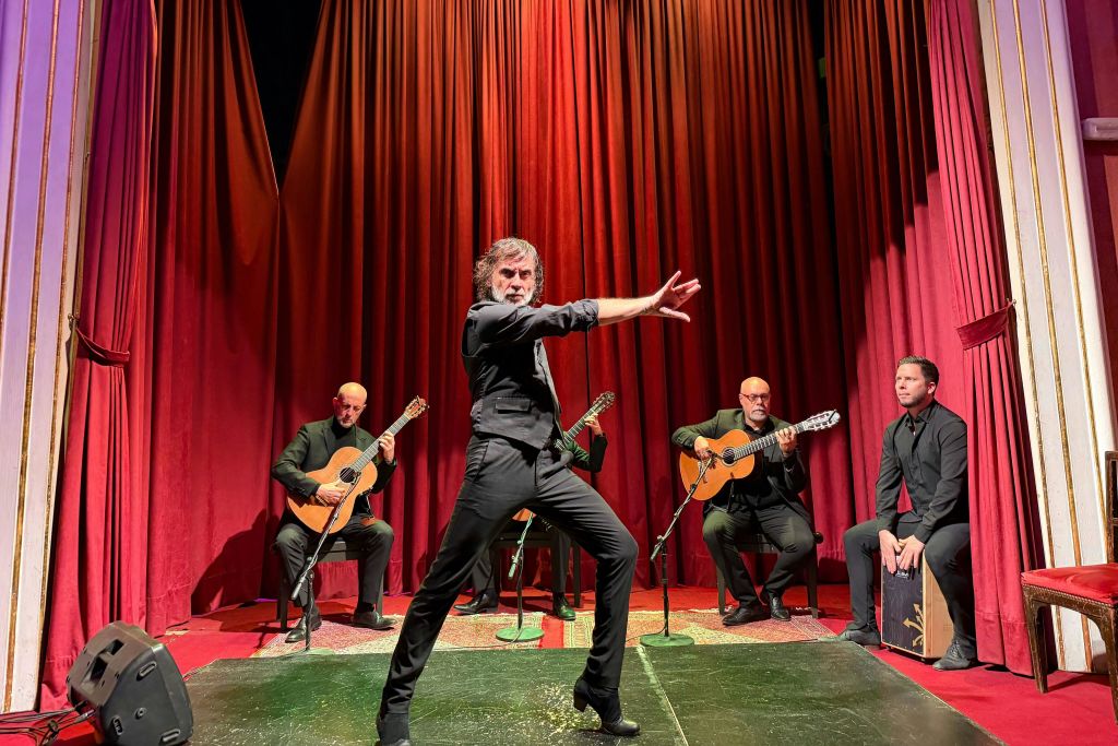 플라멩코 댄서가 세 명의 기타리스트와 타악기 연주자 앞에서 빨간색 커튼으로 무대를 장식합니다.