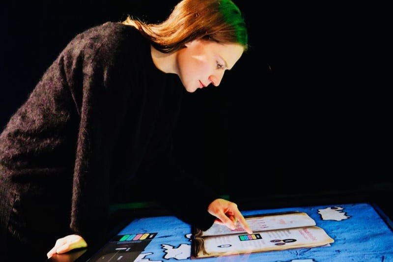 어두운 환경에서 다채로운 그래픽을 보여주는 디지털 터치스크린 디스플레이와 상호 작용하는 사람.