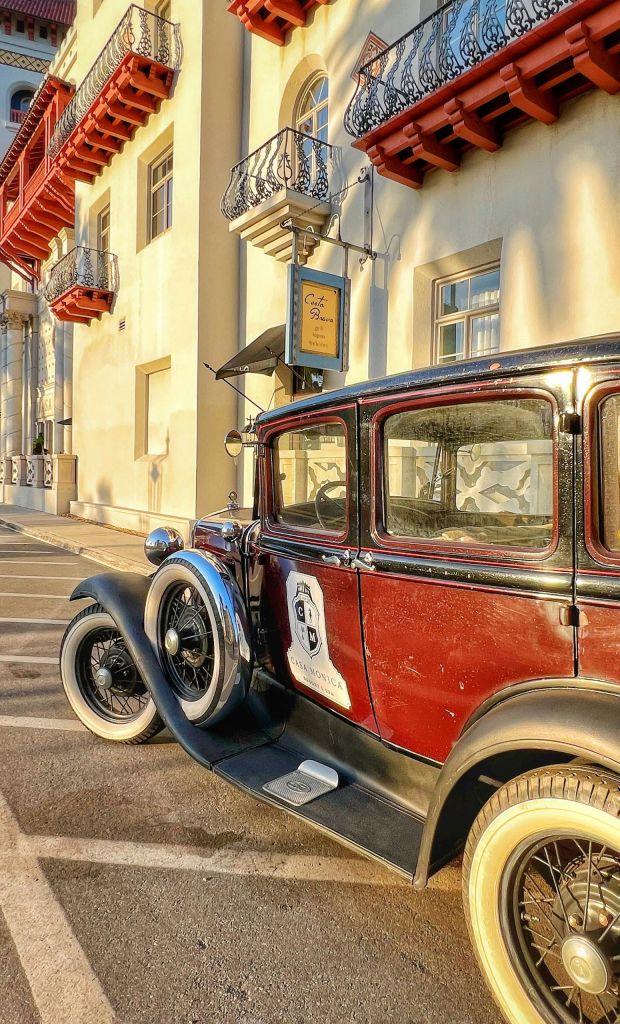 건물 옆에 "Corte dei Pini" 라고 적힌 표지판과 위에 보이는 장식 발코니가 있는 빈티지 차량이 주차되어 있습니다.