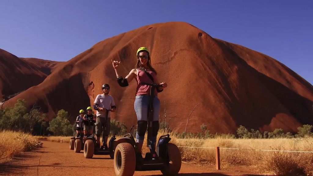 커다란 붉은 바위 지층을 배경으로 사막에서 세그웨이를 타는 네 명의 사람들.