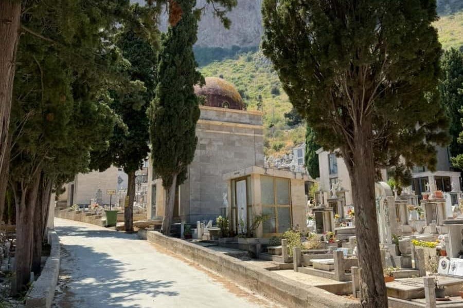 높은 편백나무와 여러 개의 묘비, 그리고 언덕을 배경으로 맑은 하늘 아래 돔이 있는 묘지가 있습니다.