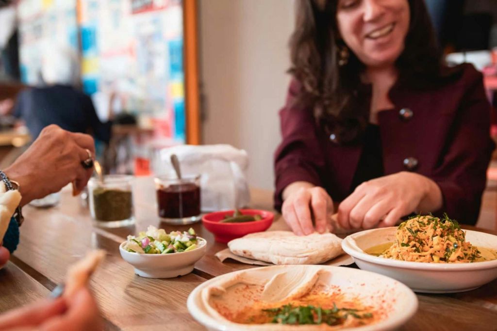 편안한 분위기에서 디핑 소스, 피타 빵, 후무스 한 접시를 곁들인 테이블에서 미소를 지으며 음식을 준비하는 사람.