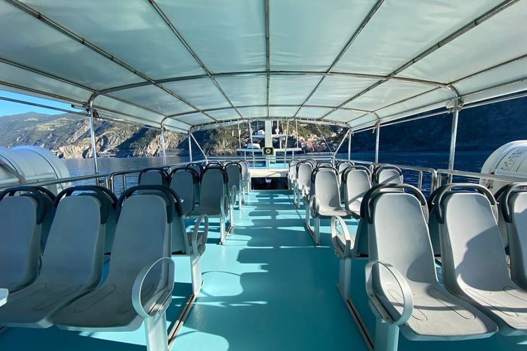 물과 해안 절벽이 배경으로 내려다보이는 캐노피 아래 회색 좌석이 줄지어 있는 빈 보트 데크의 모습.