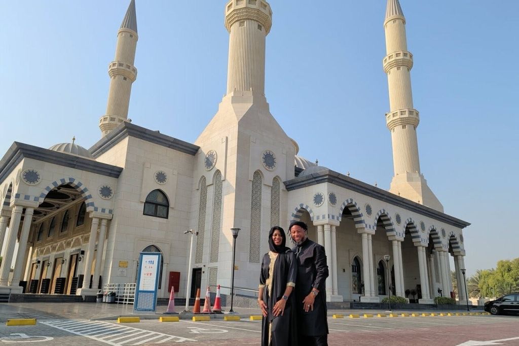 화창한 날 높이 솟은 첨탑과 아치형 입구가 있는 모스크 앞에 한 남녀가 서 있습니다.