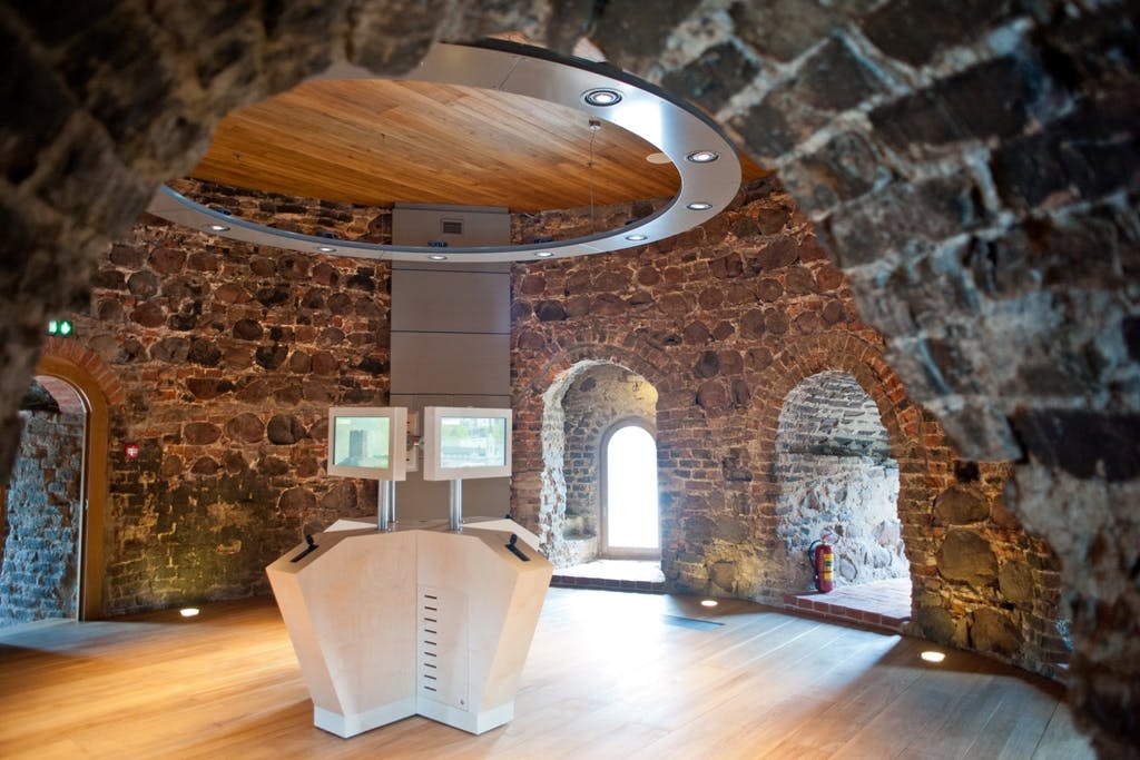 아치형 천장이 있는 석조 벽 건물의 내부에는 두 개의 스크린과 원형 조명 기구가 있는 현대적인 정보 키오스크가 있습니다.