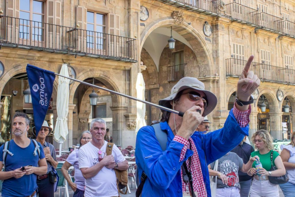 유서 깊은 광장에서 가이드 투어를 진행하는 일행으로, 가이드가 깃발을 들고 전경에 태양 모자를 쓰고 있습니다.