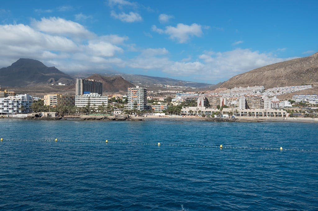 해안 지역을 따라 건물이 있는 도시 스카이라인, 전경의 푸른 바다, 부분적으로 흐린 하늘 아래를 배경으로 한 산.