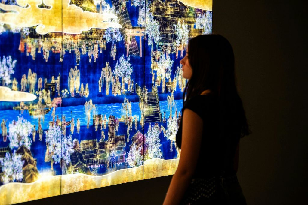 정교한 패턴과 생생한 색감이 돋보이는 밝게 빛나는 작품 앞에 한 사람이 서 있습니다.