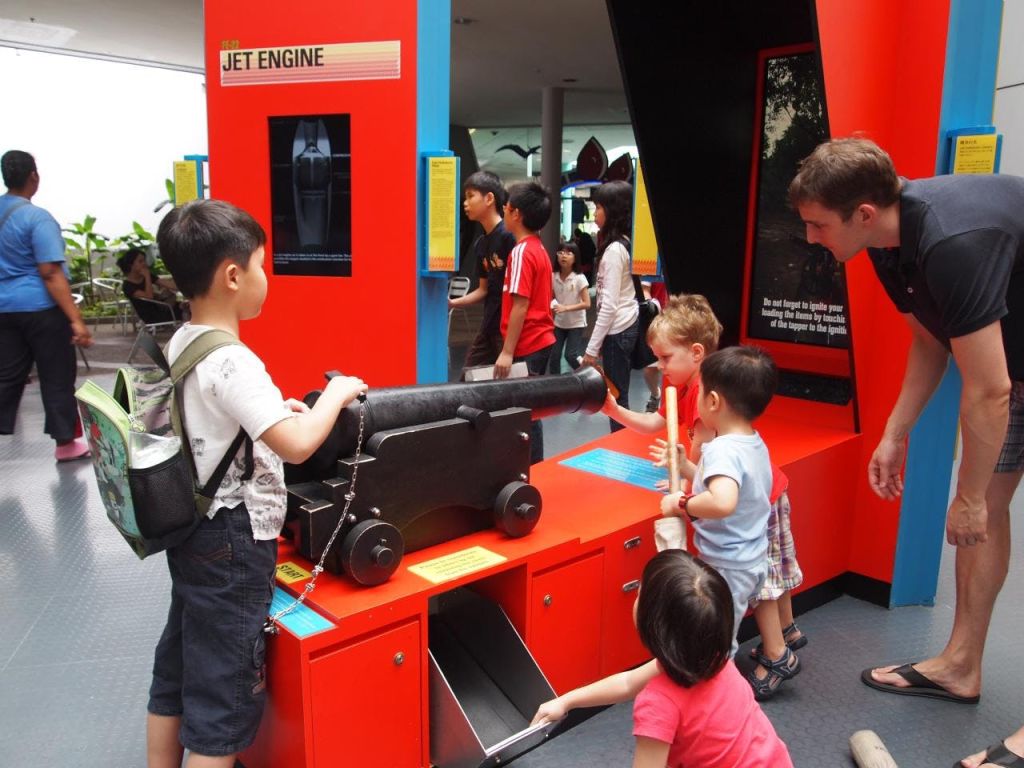 성인과 어린이는 다채로운 실습 과학 박물관 전시회에서 대포를 포함한 전시물과 상호 작용합니다.