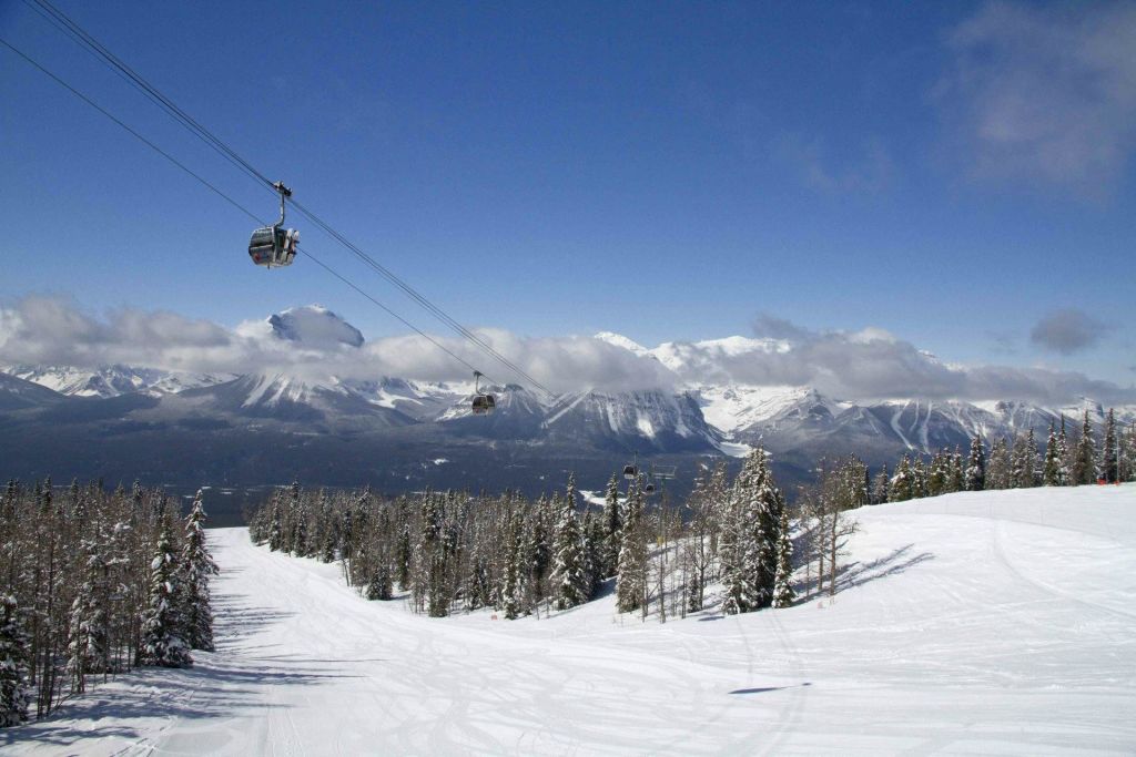 눈 덮인 슬로프, 상록수, 설산과 푸른 하늘을 배경으로 한 케이블카가 있는 스키 리조트.