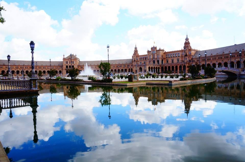 부분적으로 흐린 푸른 하늘 아래, 고요한 수체에 비친 탑과 아치가 있는 거대한 역사적인 건물.