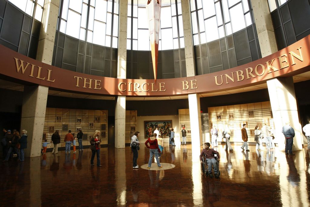 사람들은 높은 창문이 있는 크고 햇살이 비치는 아트리움에서 걷고 모입니다. "THE CIRCLE BE UNBRO" 라는 원형 문구가 새겨져 있습니다.