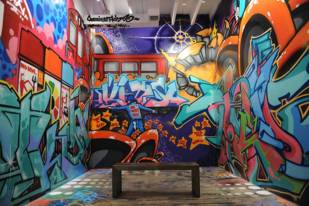 마모된 바닥 중앙에 나무 벤치가 있고, 추상적인 디자인과 모양이 돋보이는 화려한 그래피티 아트로 장식된 객실입니다.