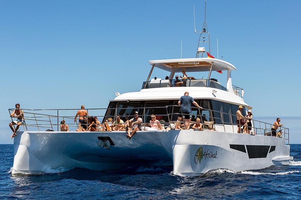 맑은 하늘 아래 푸른 바다를 항해하는 '아프리캇 (Afrikat)' 이라는 이름의 하얀 요트 갑판에서 휴식을 취하며 일광욕을 즐기는 사람들.