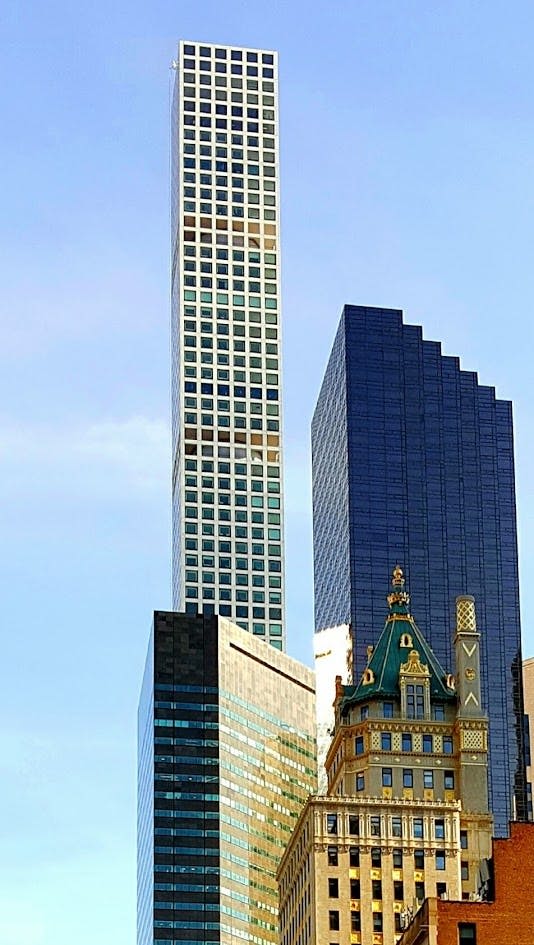 현대적인 고층 건물, 푸른 유리 건물, 맑은 하늘 아래 화려한 녹색 지붕 구조가 특징인 도시 풍경.