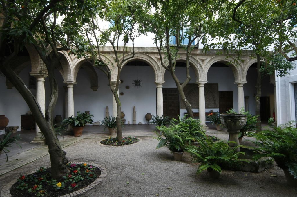 아치, 나무, 화분, 양치식물이 있는 마당으로 자갈로 덮인 땅과 전경에 작은 화단이 있습니다.