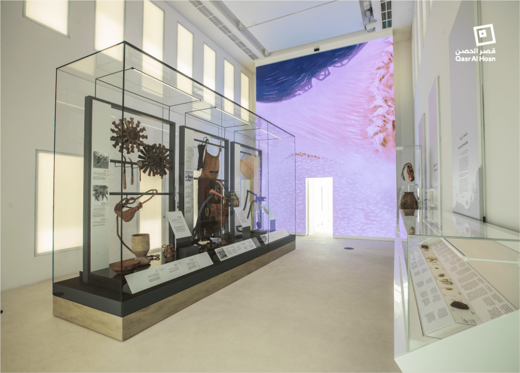 유리 케이스의 유물, 서술된 명판, 뒷벽의 커다란 추상적 이미지를 보여주는 박물관 전시관입니다.