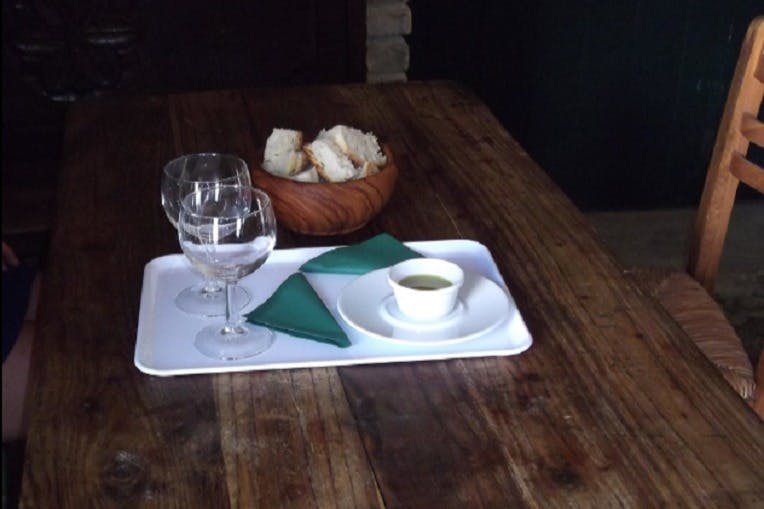 두 개의 빈 와인 잔, 작은 수프 한 그릇, 녹색 냅킨을 담은 흰색 트레이가 있는 나무 테이블 세트. 근처에는 빵 한 그릇이 있습니다.