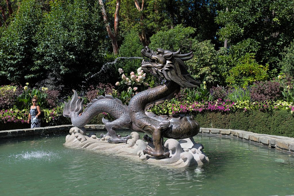 울창한 녹음으로 둘러싸인 작은 연못의 청동 용 조각상과 정원의 꽃 식물.