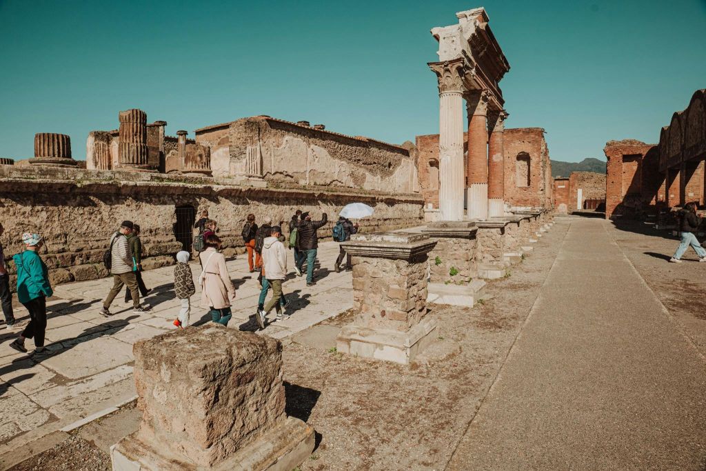 관광객들은 맑고 푸른 하늘 아래 석조 기둥과 벽돌이 있는 고대 유적을 거닐고 있습니다.