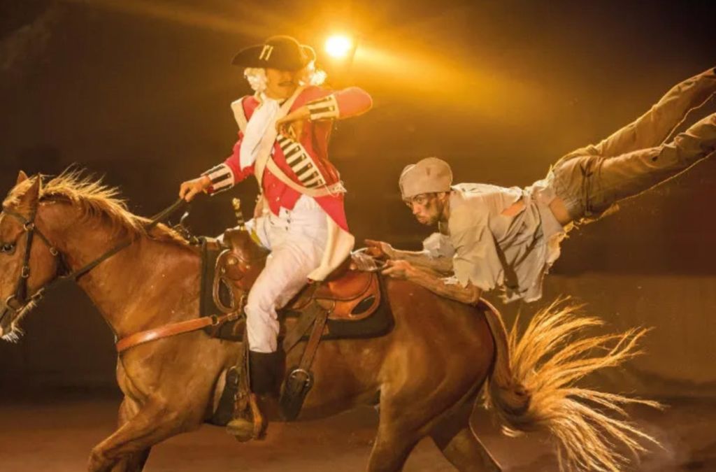붉은 군복을 입은 사람이 말을 타고, 또 다른 사람이 극적인 장면에서 안장에 매달려 있습니다.