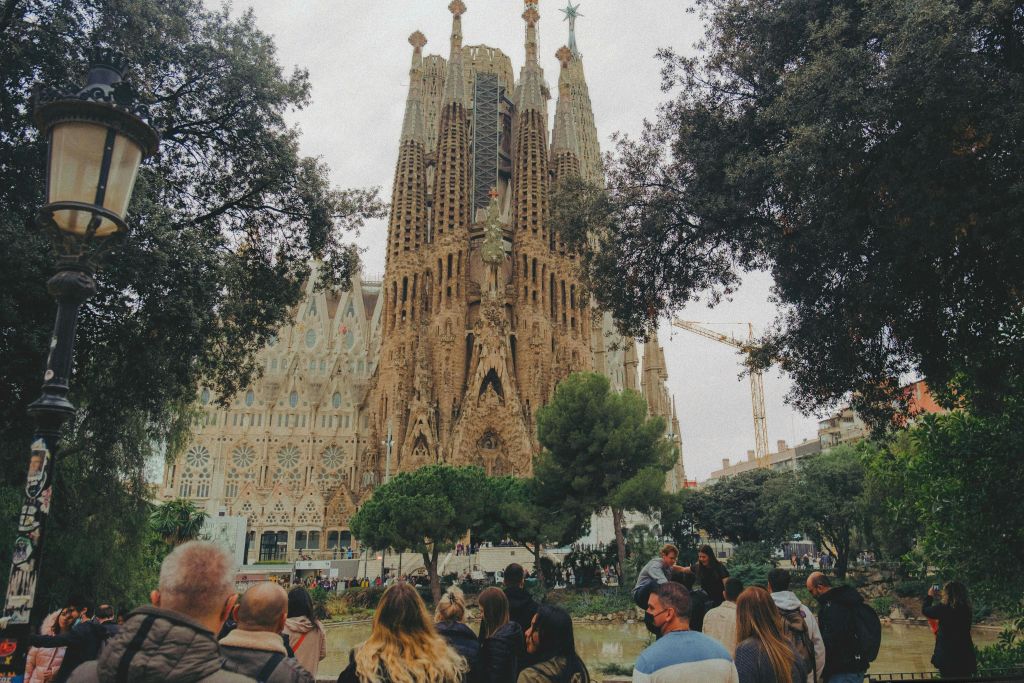 바르셀로나의 사그라다 파밀리아 (Sagrada Família) 대성당이 나무로 둘러싸인 연못 근처에 많은 사람들이 모여들었습니다.