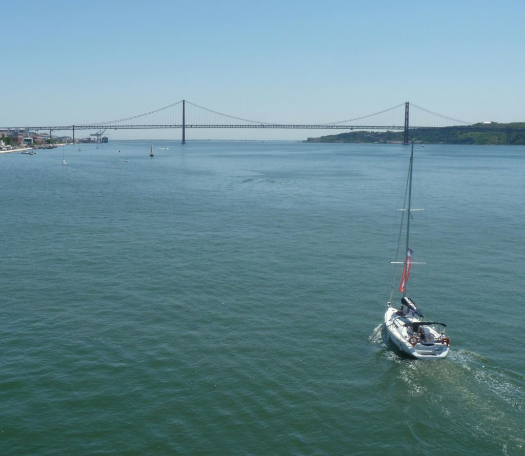 맑고 푸른 하늘 아래 먼 현수교를 향해 잔잔한 물 위를 이동하는 범선.