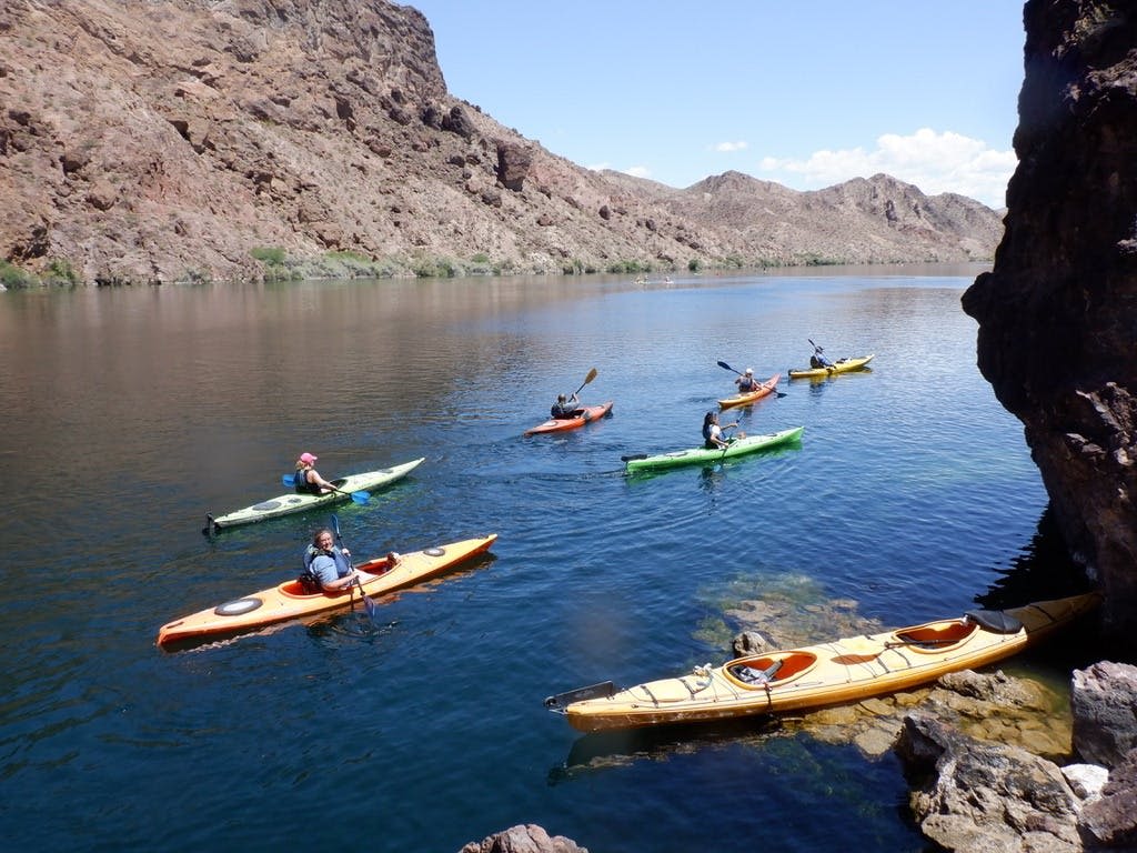 맑고 푸른 하늘 아래 바위 언덕으로 둘러싸인 잔잔한 호수에서 카약을 타는 한 무리의 사람들.
