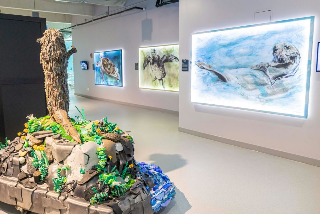 벽에 조명을 밝힌 수중 테마 예술품과 전경에 해양 생물 요소가 있는 조각된 디스플레이가 있는 갤러리 장면.