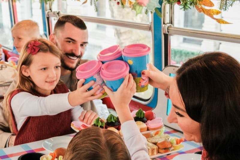 버스에 음식과 장식이 놓인 테이블에서 아이들과 어른이 행복하게 다채로운 컵을 찰칵거리고 있습니다.