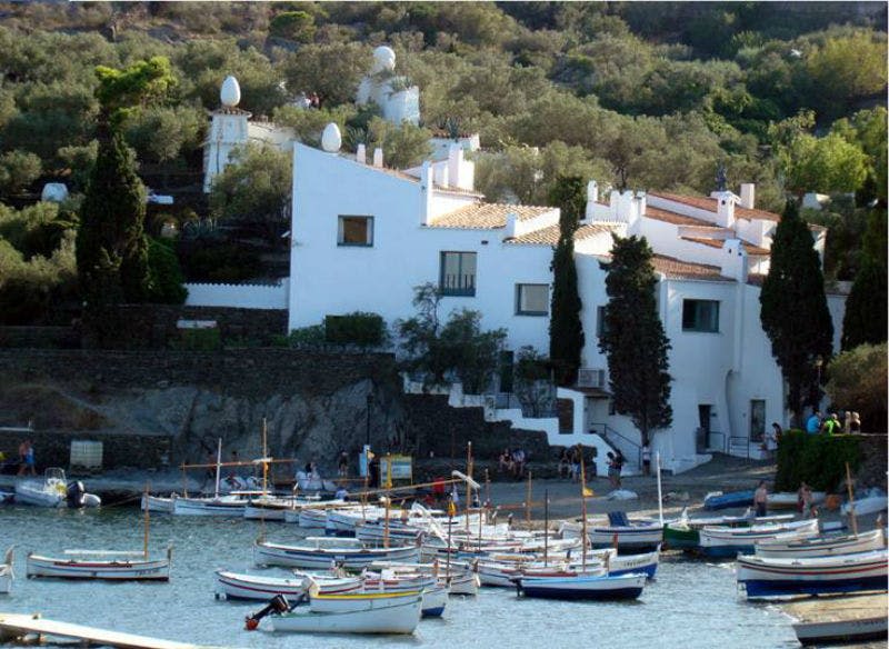 나무와 녹음이 우거진 언덕에 세워진 하얀 건물 앞 바다에 정박한 작은 보트.