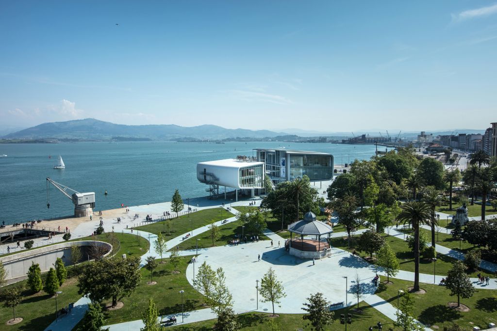 나무, 통로, 정자가 있는 공원이 내려다보이는 현대적인 수변 건물입니다. 이 장면은 산과 물을 배경으로 합니다.