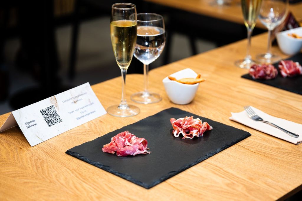 경화 고기 두 조각, 샴페인 한 잔, 물 한 잔, 브레드스틱이 담긴 작은 그릇이 담긴 검은색 슬레이트 접시.