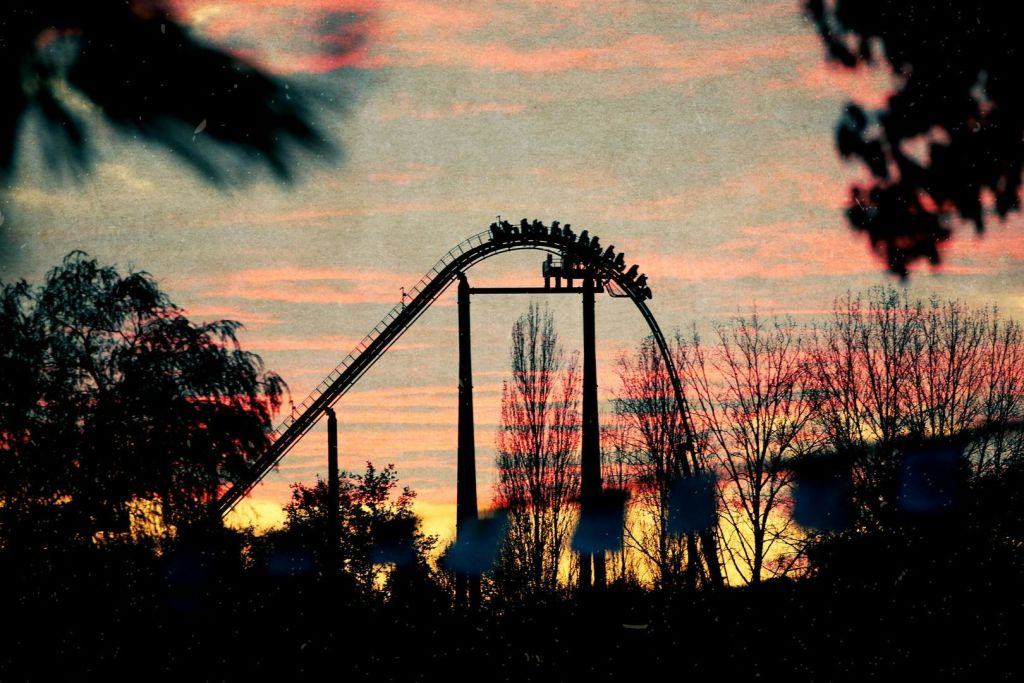 나무로 둘러싸인 활기찬 일몰 하늘을 배경으로 실루엣의 라이더가 달린 롤러코스터.