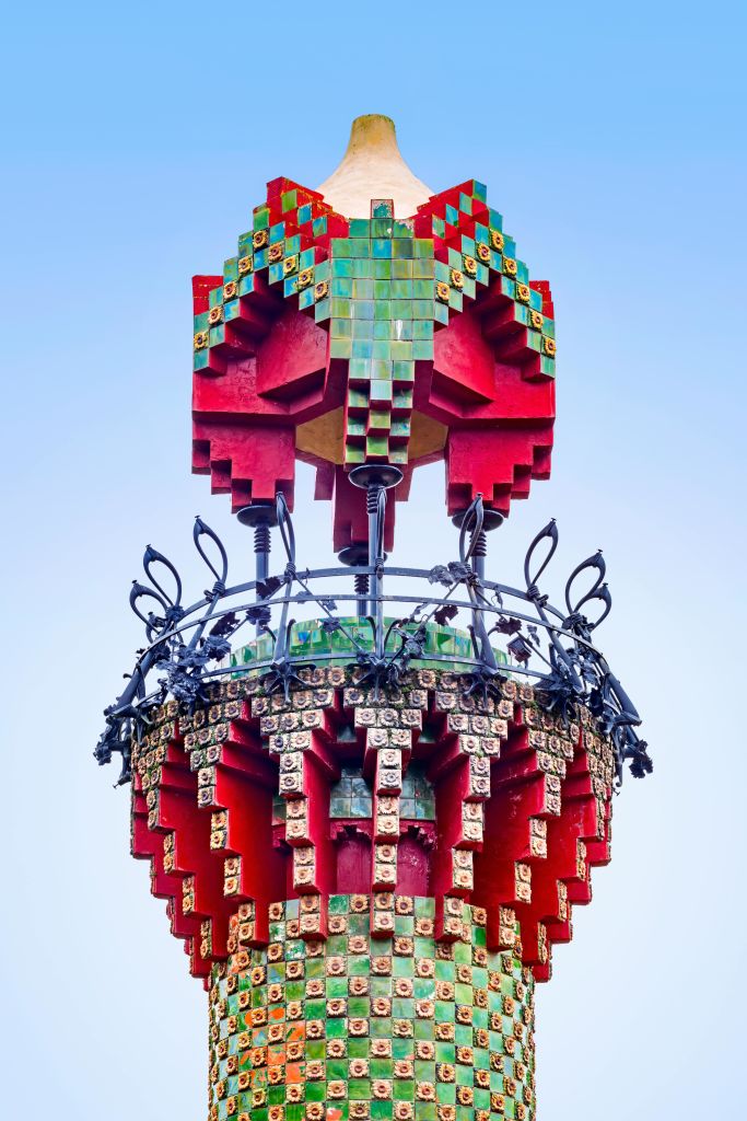 빨간색, 녹색, 금색 모자이크 패턴과 정교한 검은색 철공예품이 선명한 파란색 하늘을 배경으로 화려한 건축 디테일이 돋보입니다.