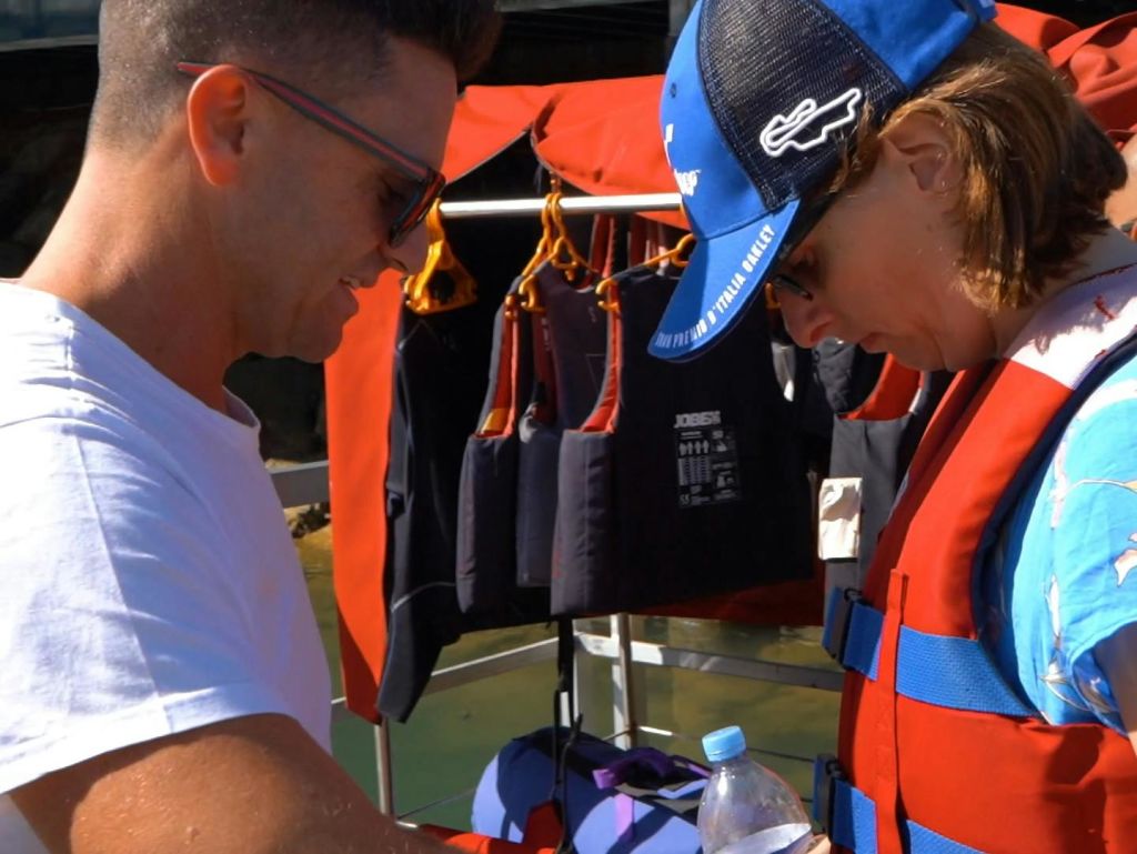 두 사람이 갈고리 근처에 구명조끼를 입고 더 많은 구명조끼를 들고 물놀이를 준비하고 있습니다. 한 사람이 물병을 들고 있습니다.