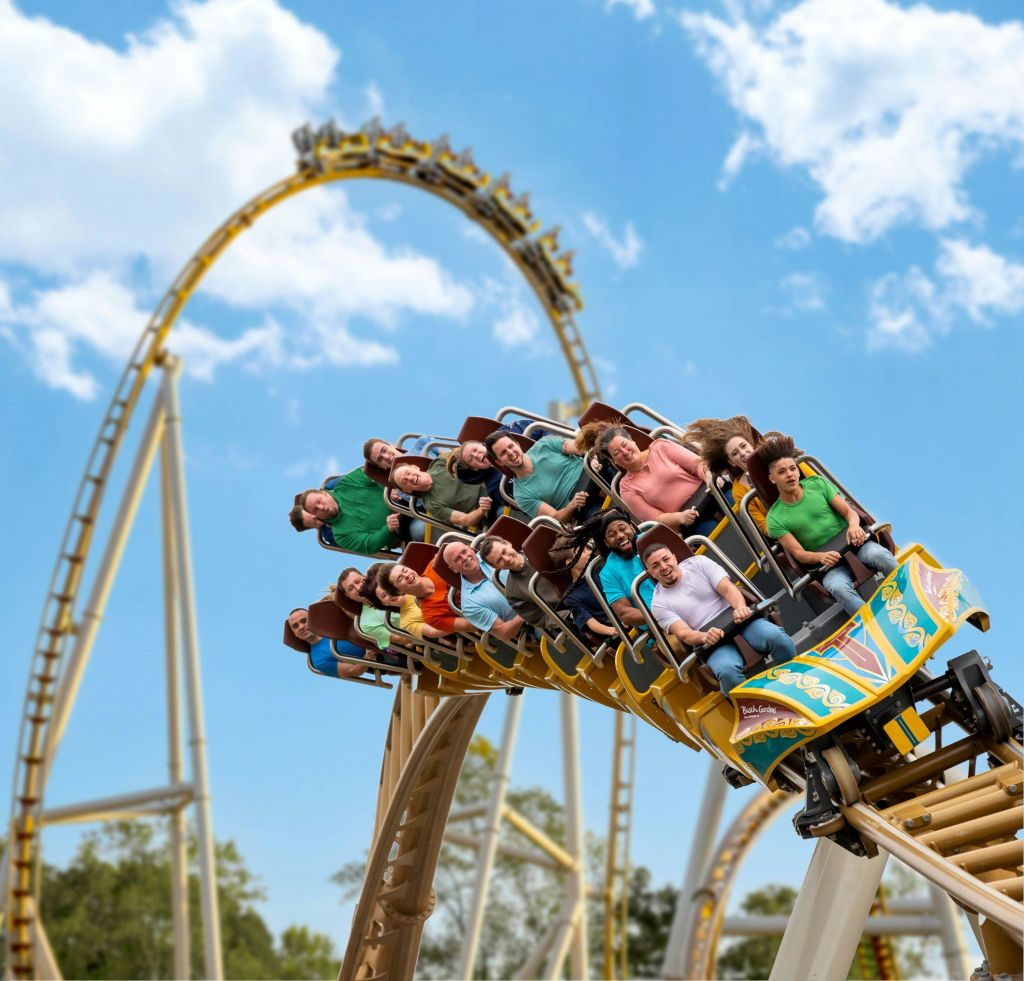 롤러코스터를 탄 사람들은 푸른 하늘과 흩어져 있는 구름을 배경으로 손을 들고 가파른 곡선을 타고 내려갑니다.