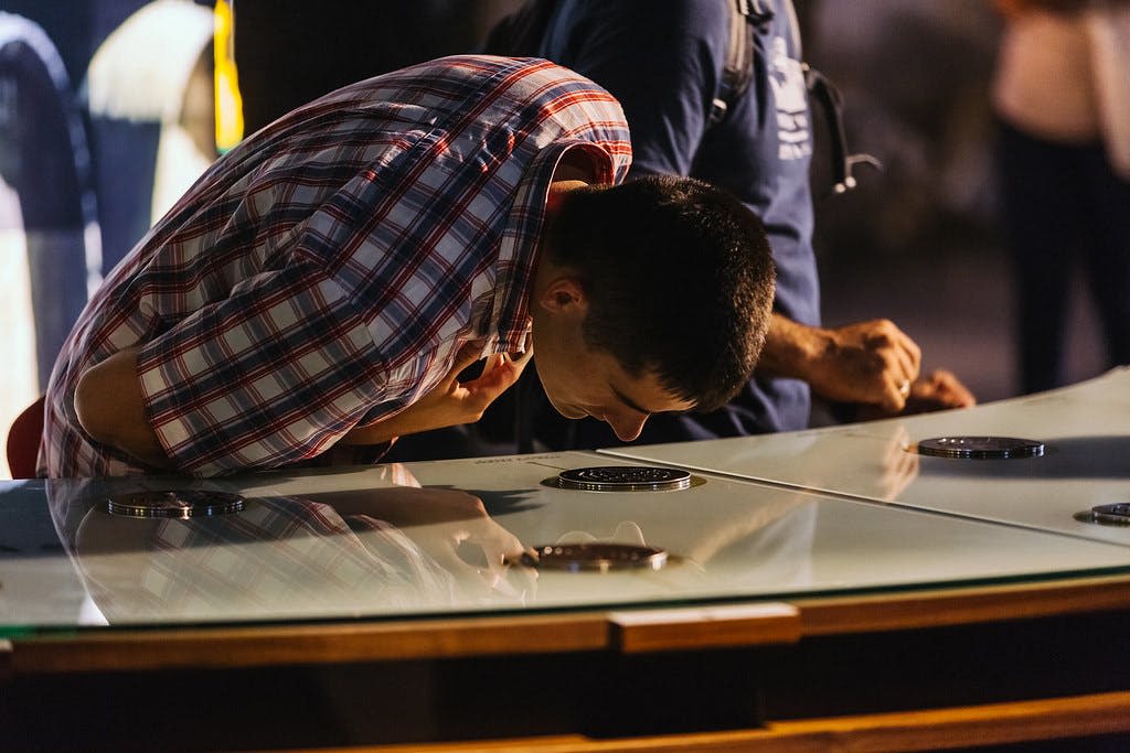 체크무늬 셔츠를 입은 남성이 유리 디스플레이에 기대어 내용을 면밀히 검사하고 있습니다. 다른 사람이 근처에 서 있습니다.