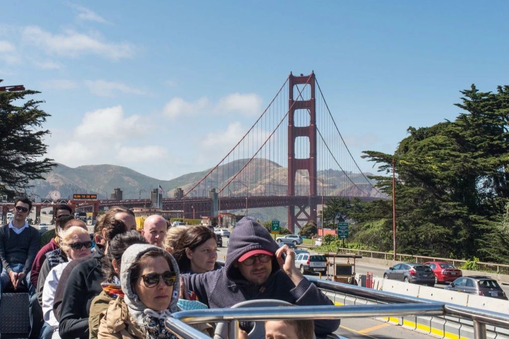 금문교와 언덕을 배경으로 투어 버스를 탄 사람들. 구름이 흩날리며 하늘이 맑다.