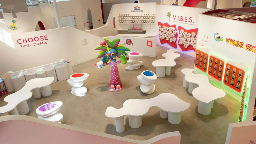 곡선형 흰색 테이블, 독특한 좌석, 벽에 "V.I.B.E.S." 라고 표시된 컵을 들고 있는 장난스러운 야자수 조각이 있는 다채로운 실내 장면.