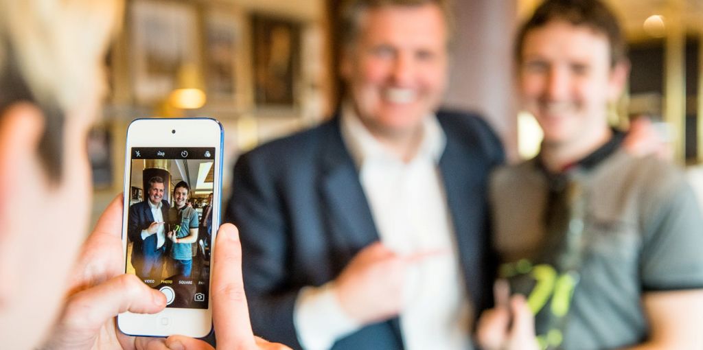 양복을 입은 두 남자가 미소를 짓고 한 남자가 다른 남자를 가리키고 있는 스마트폰 화면의 클로즈업.