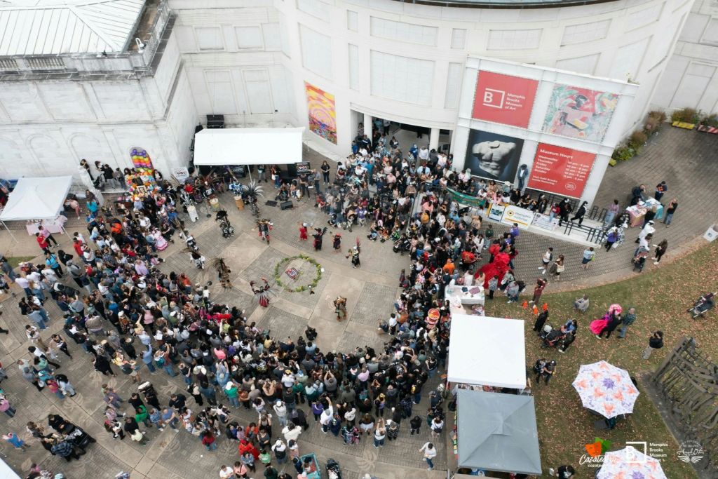 포스터가 붙은 하얀 건물 바깥 중앙 공연장 주변에 모여든 많은 인파의 공중 전경.