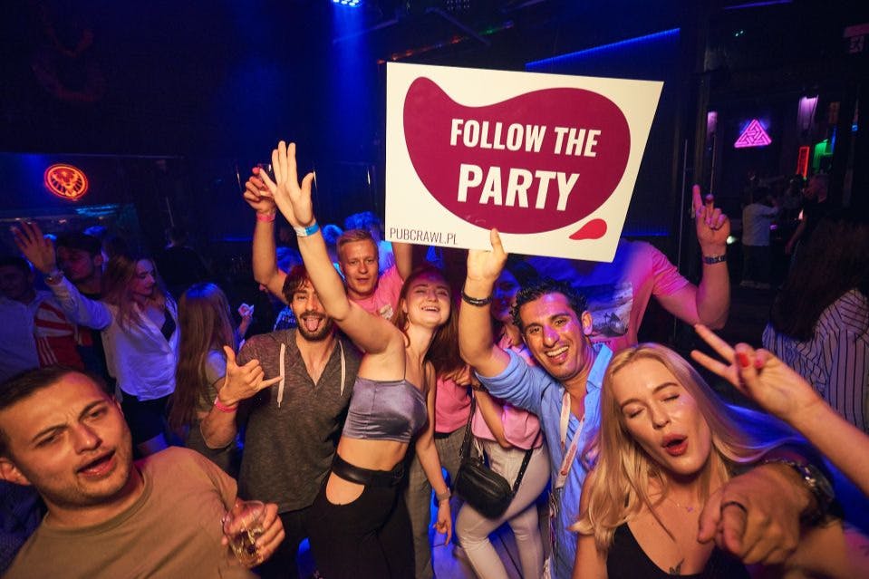 "Follow the Party - pubcrawl.pl" 사인이 있는 단체 셀카를 찍기 위해 포즈를 취하는 펍 크롤링 참가자 그룹