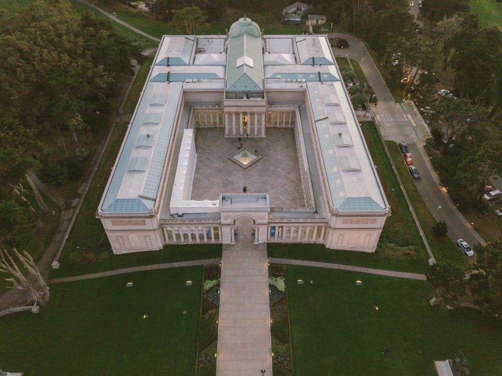 녹지로 둘러싸인 중앙 안뜰과 주차된 자동차가 있는 인접한 도로가 있는 커다란 U자형 건물의 공중 전망.