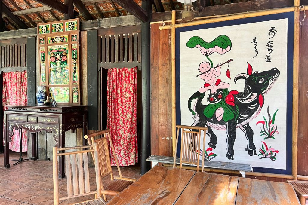 붉은 꽃무늬 커튼, 테이블 주위에 나무 의자, 검은 황소 위에 어린이가 그려진 벽이 있는 전통적인 목조 객실입니다.