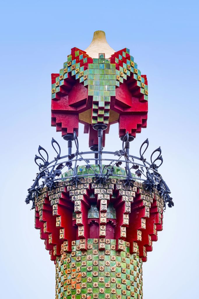 빨간색, 녹색, 금색 모자이크 패턴과 정교한 검은색 철공예품이 선명한 파란색 하늘을 배경으로 화려한 건축 디테일이 돋보입니다.