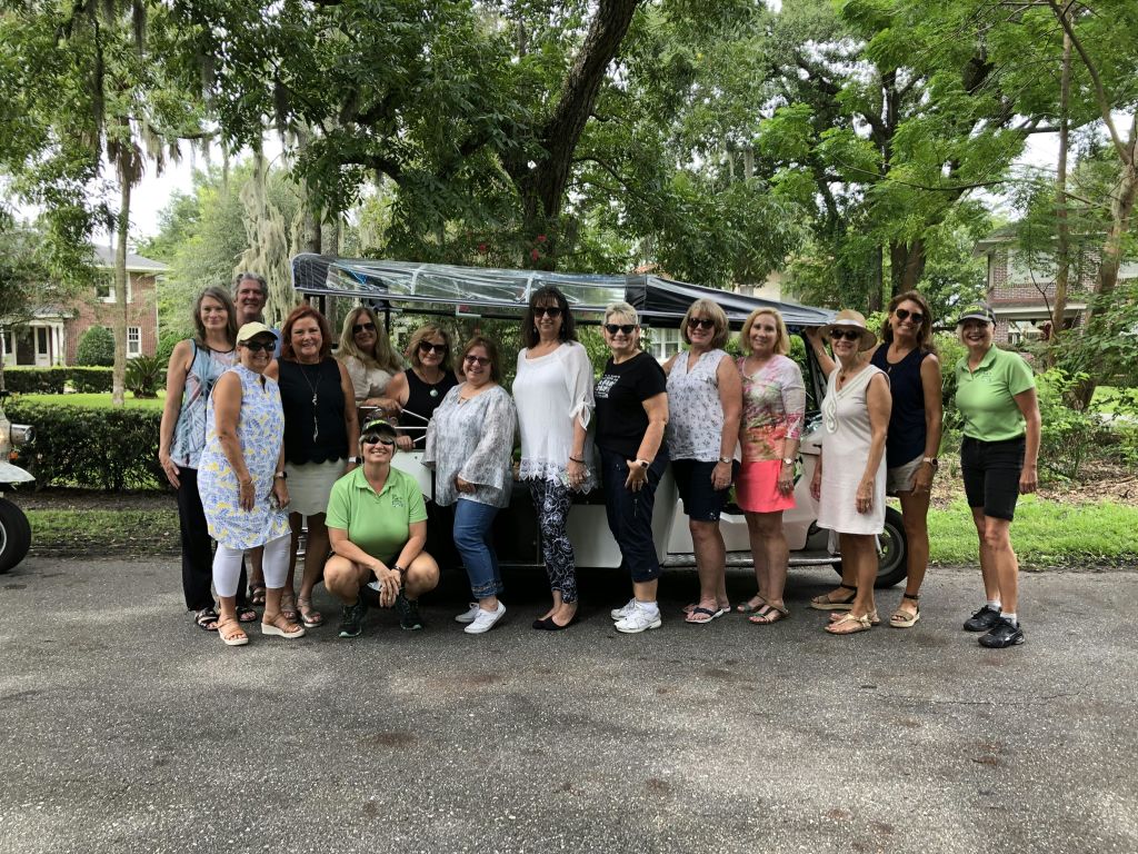 가로수 길에서 흰색 차량 앞에서 포즈를 취하고 있는 한 무리의 사람들. 한 사람은 웅크리고, 다른 사람은 서 있습니다.