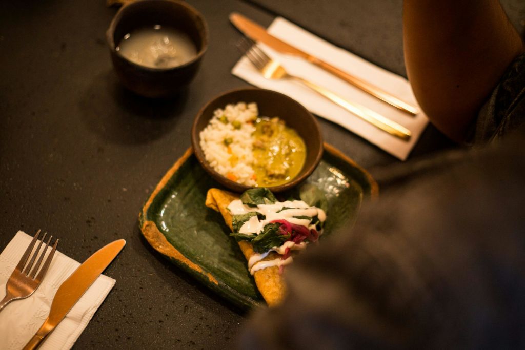 야채와 소스를 얹은 타코, 밥과 카레 한 그릇, 어두운 테이블에 놓인 음료 한 잔이 담긴 접시.