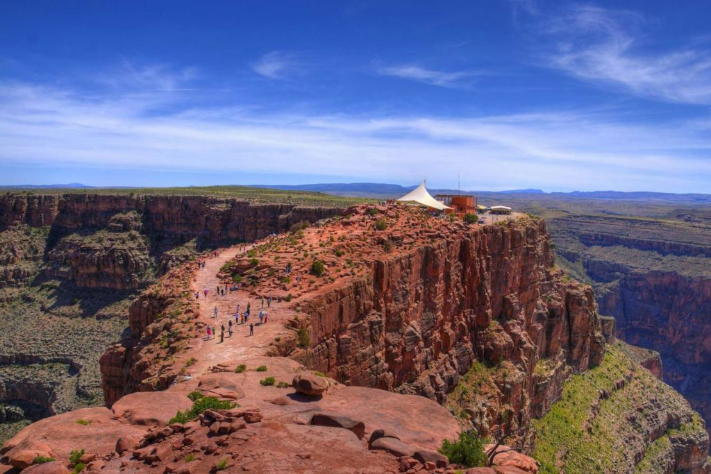 푸른 하늘 아래 텐트를 치고 건물을 배경으로 바위 절벽 위를 걷고 있는 한 무리의 사람들.