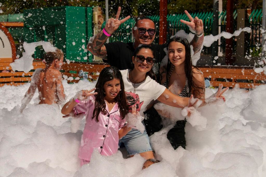 거품이 가득한 야외 공간에서 미소 짓고 포즈를 취하는 네 명의 사람들이 손으로 평화의 표지판을 만들고 있습니다.